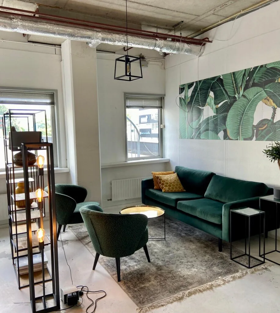 Modern ingerichte zithoek aan de Anthony Fokkerweg met groene meubels, een tropisch wandpaneel en industriële accenten.